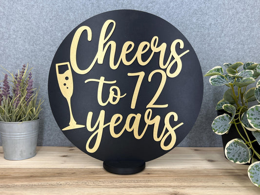 a black and gold sign that says cheers to 72 years